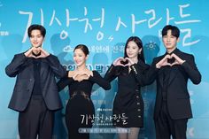 three people standing in front of a blue wall making heart shapes with their hands while wearing black suits