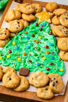 a christmas tree made out of cookies sitting on top of a wooden cutting board with green frosting and sprinkles