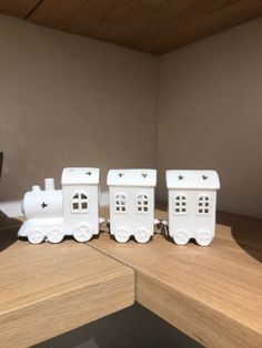 three white train engines sitting on top of a wooden table next to a black vase