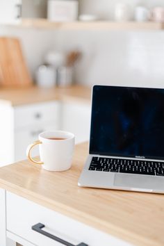 an open laptop computer sitting on top of a wooden table next to a cup of coffee