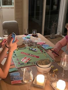 two women sitting at a table playing a game with their cell phones and wine glasses