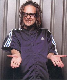 a man with dreadlocks and sunglasses standing in front of a metal wall holding his hands out