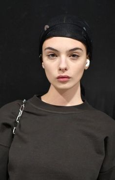 a woman in a black top with a chain around her neck and wearing a beanie