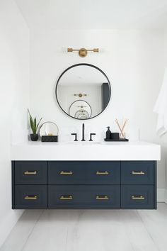 a bathroom vanity with two sinks and a large round mirror above it, in front of a white wall