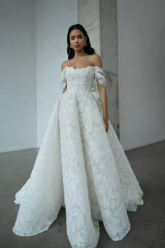 a woman in a white wedding dress standing next to a columned wall and wearing an off - the - shoulder gown