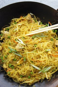 a wok filled with noodles and vegetables next to chopsticks