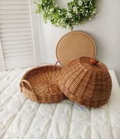 two wicker baskets sitting on top of a white bed next to a round mirror