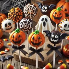 halloween cake pops with pumpkins, bats and ghost faces on them sitting on a wooden table