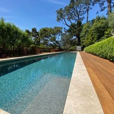 an empty swimming pool surrounded by greenery and wooden decking in the middle of a garden