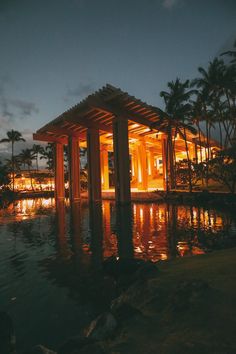 an outdoor pavilion lit up at night with lights reflecting off the water and palm trees in the background