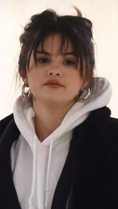 a woman in black and white hoodie looking off to the side with her hair pulled back