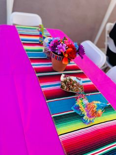 the table is set up with bright colors and flowers in vases on top of it