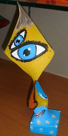 a yellow sculpture with blue eyes on top of a wooden table