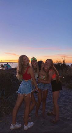 three girls are standing on the beach at sunset