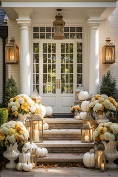 white pumpkins and yellow flowers are on the steps in front of a house with lanterns