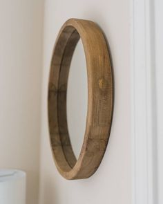 a round wooden mirror mounted to the side of a white wall next to a vase