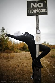 a person leaning up against a pole with a no trespassing sign on it