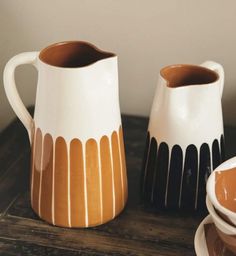 two brown and white pitchers sitting on top of a table next to a plate with a spoon