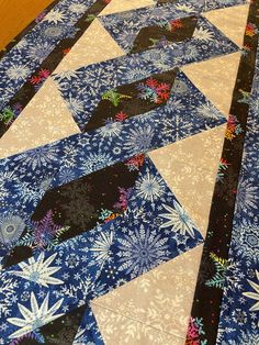 a blue and white quilt with snowflakes on the top is laying on a wooden floor