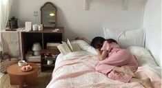 a woman laying in bed with her head on the pillow while reading a book and drinking coffee