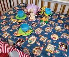 a baby's crib with a blue table cloth covered in tea cups and giraffe figurines