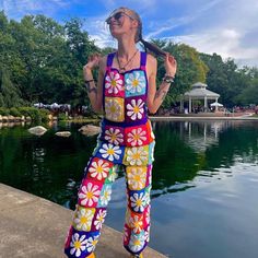 a woman standing on the edge of a body of water wearing colorful pants and sunglasses