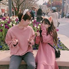 two people sitting on a bench in front of flowers and tulips with one person covering his eyes