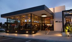 people are standing outside the entrance to a restaurant at night with lights shining on the windows