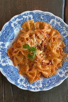 a blue and white plate filled with pasta on top of a wooden table next to a fork