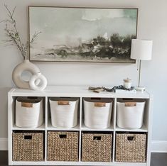 a white shelf with baskets on it and a painting hanging above the shelves in front of it