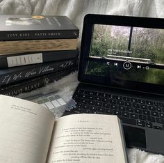 an open laptop computer sitting on top of a bed next to books and other items