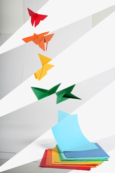 an origami bird is flying in the air over folded paper and colored papers