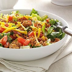 a salad with meat, cheese and lettuce in a white bowl on a table