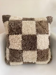 a brown and white patchwork pillow sitting on top of a white chair next to a wall