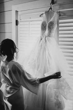 a woman looking at a wedding dress hanging on a window sill