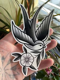 a hand holding up a sticker with a bird on it's head and flowers in the background