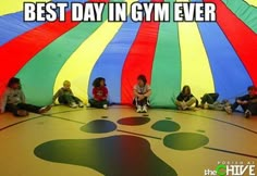 several children sitting on the floor in front of a large colorful umbrella with paw prints