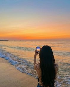 a woman standing on top of a beach holding a cell phone