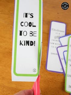 a hand holding a pair of pink scissors next to some cards with words on them