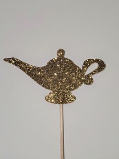 a cake topper that looks like a teapot on a stick with gold glitter