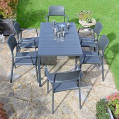 an outdoor table and chairs set up on a stone patio with grass in the background