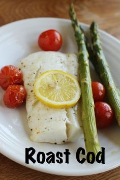 a white plate topped with fish and asparagus next to tomatoes on top of a wooden table