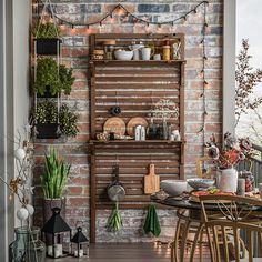 an outdoor dining area with brick walls and potted plants on the shelves, along with wooden chairs