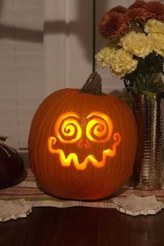 a carved pumpkin sitting on top of a wooden table next to flowers and vases