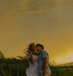 a man and woman standing in tall grass with the sun setting behind them, making faces at each other