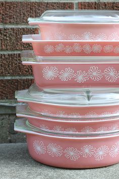 pink glass casserole dishes stacked on top of each other in front of a brick wall