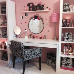 a desk with a mirror, chair and shelves in a room that has pink walls