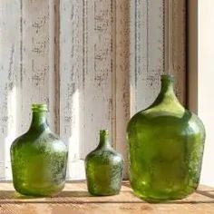 three green glass vases sitting on top of a wooden table next to a window