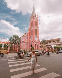 a woman crossing the street in front of a pink church