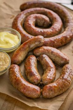 two sausages and mustard on a piece of wax paper next to some condiments